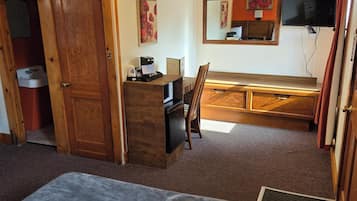 Ein Zimmer mit einem Bett, einem Schreibtisch mit Computer, einem Fernseher und einer Tür zu einem Badezimmer.