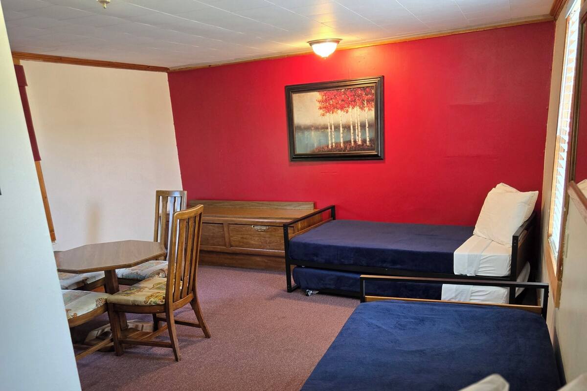 A room with two beds, a wooden desk, a chair, and a red wall.