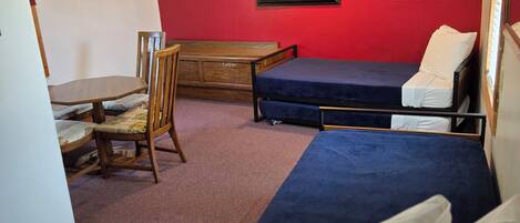 A room with two beds, a wooden desk, a chair, and a red wall.