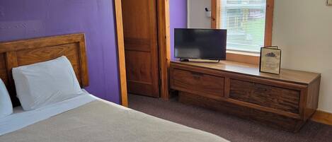 A bedroom with a bed, a dresser, a television, and a window with blinds.