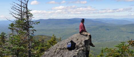A person sitting on a rock with a backpack, overlooking a mountainous landscape.
