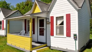 A small, single-story house with a porch, a door, and a window with red shutters.