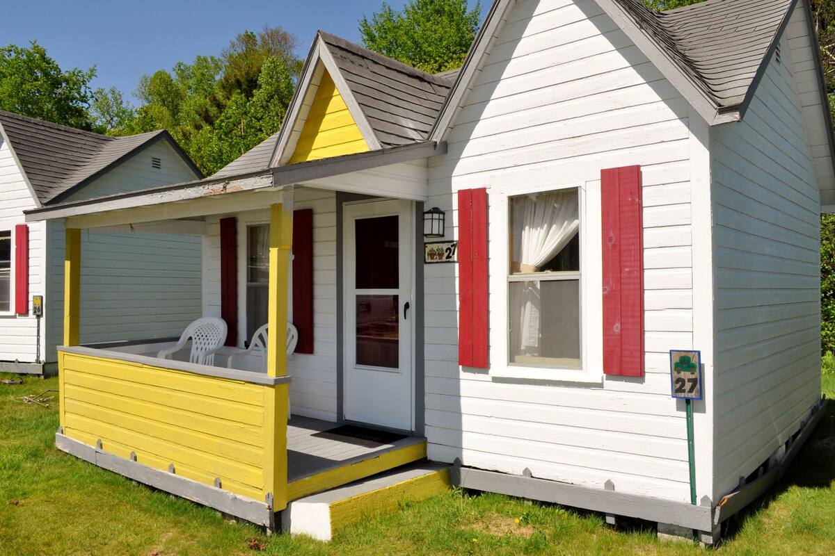 A small, single-story house with a porch, a door, and a window with red shutters.