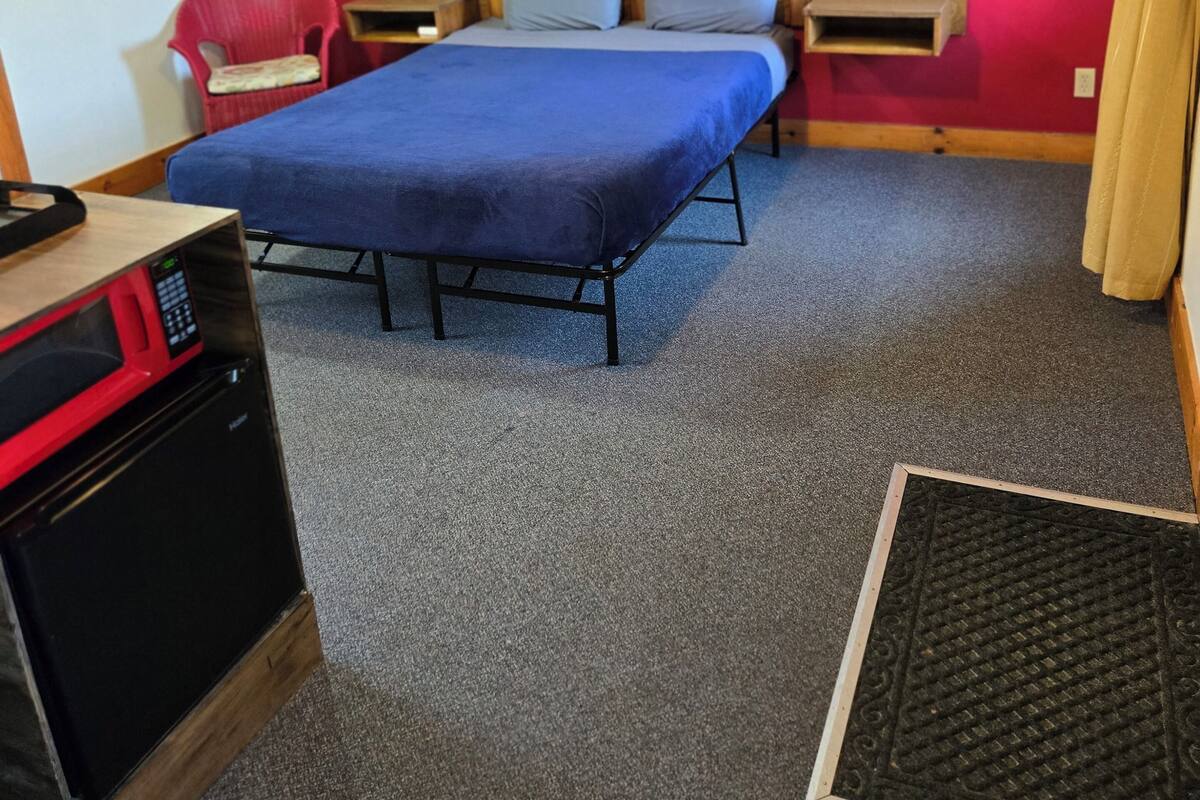A hotel room with a bed, a desk, a chair, a microwave, and a small table.