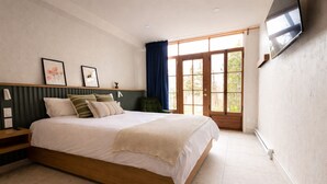 Une chambre avec un grand lit, un téléviseur fixé au mur et une fenêtre avec des rideaux.