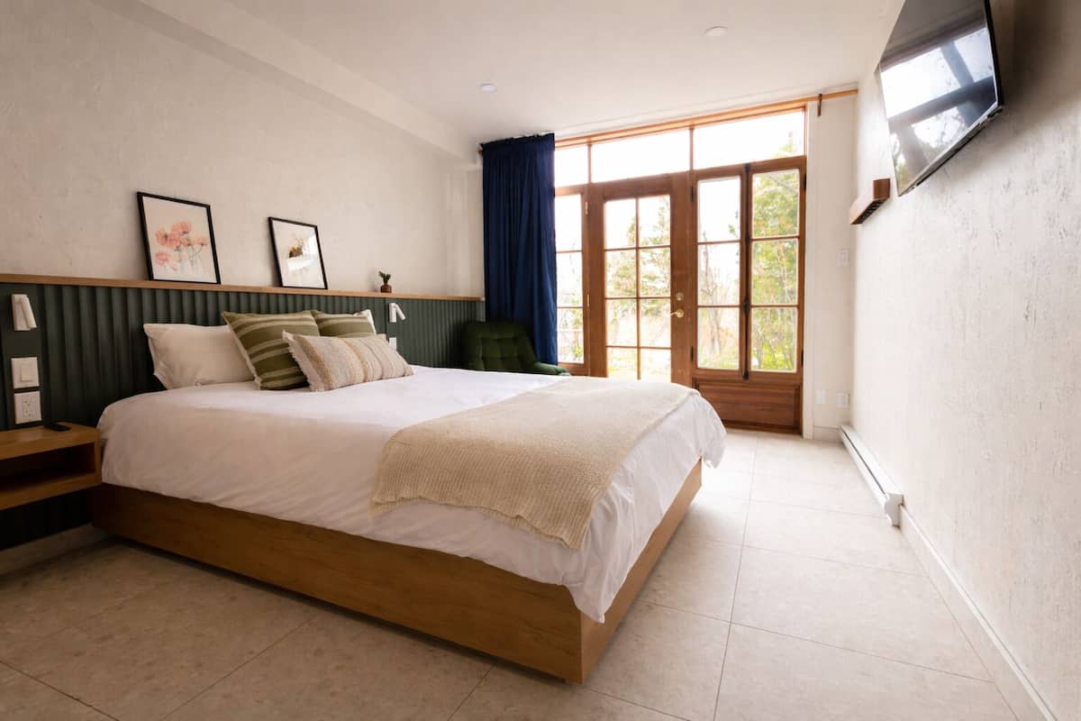 Une chambre avec un grand lit, un téléviseur fixé au mur et une fenêtre avec des rideaux.