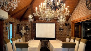 Un espace repas agrémenté d’un mur en briques, d’un plafond en bois et de lustres. Les tables sont dressées avec des nappes blanches et des chaises.