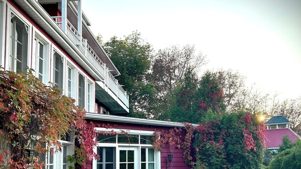 Une maison à deux étages avec un balcon, un chemin de pierre et un jardin agrémenté de plantes en pot ainsi que d’une table et de chaises.