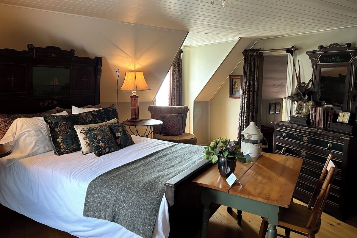 Une chambre à coucher avec un grand lit, une table sur laquelle est posé un vase, une commode et une lampe.