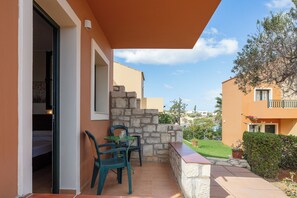 A balcony with a table and chairs, a stone wall, and a view of neighboring buildings. - Dia Apartments (Hersonissos)