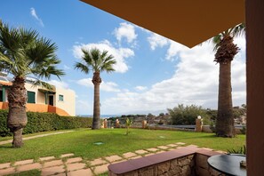 A courtyard with palm trees, a stone bench, and a view of the sea. - Dia Apartments (Hersonissos)
