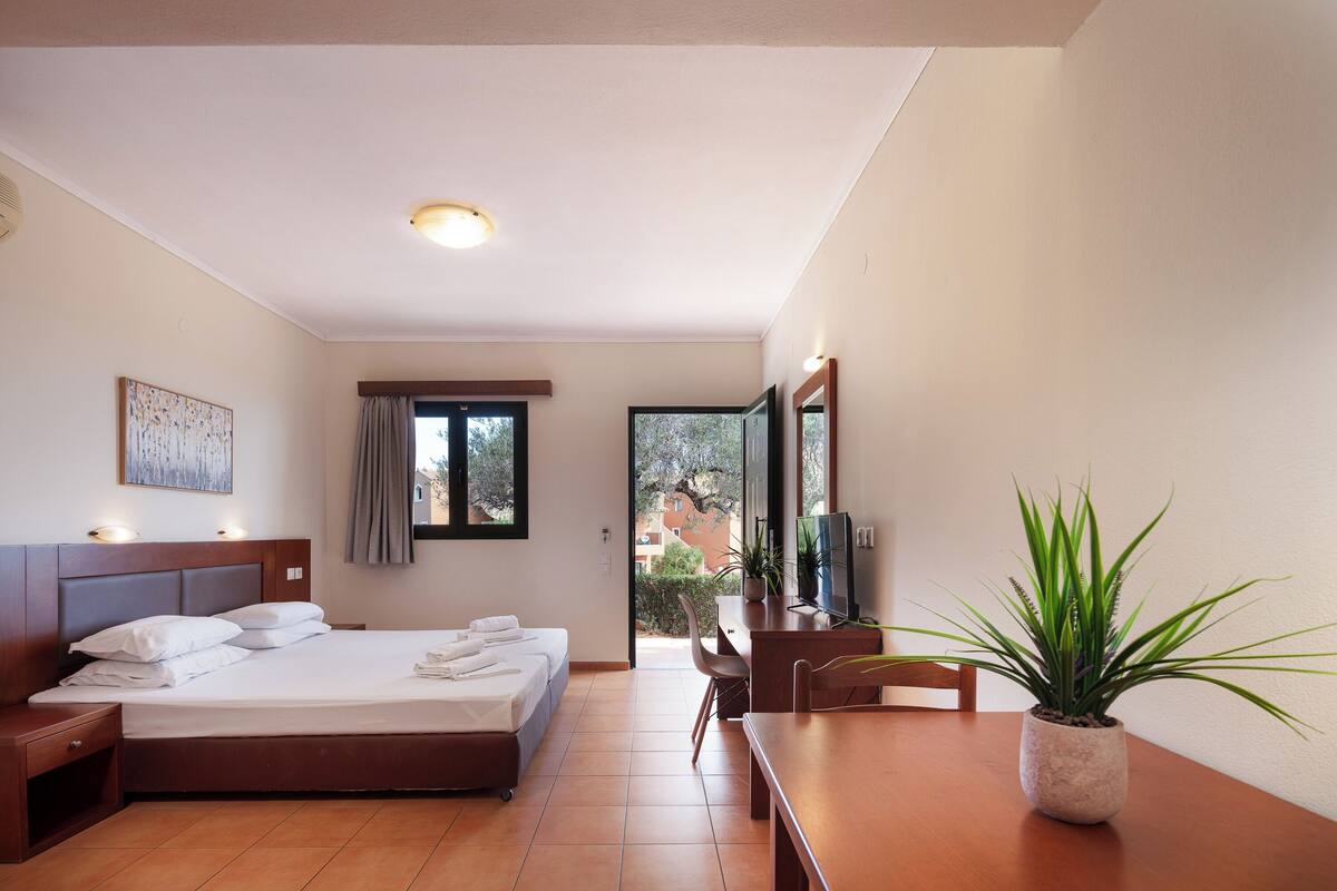 A bedroom with a bed, bedside tables, a desk, a chair, a television, and a potted plant.