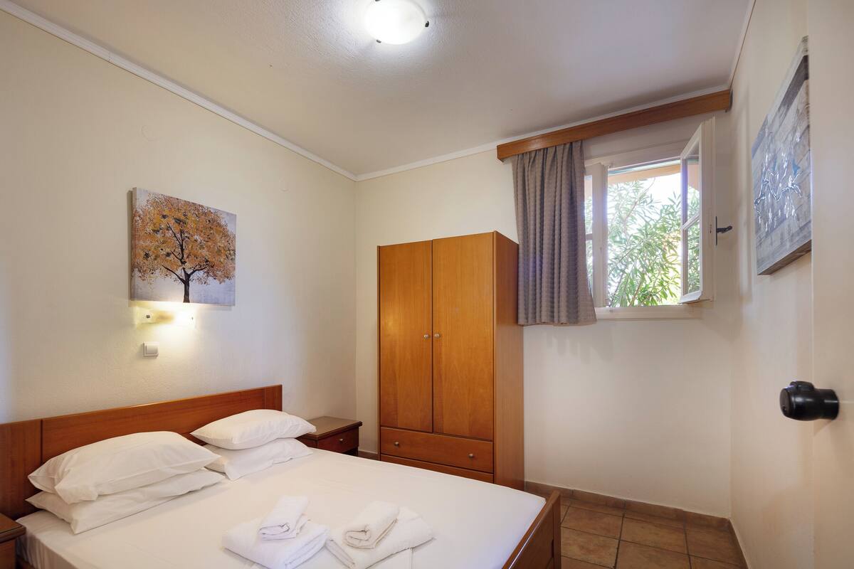 A bedroom with a bed, a wooden wardrobe, a painting on the wall, and a window with curtains.