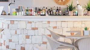 A bar area with a stone wall, wicker chairs, and a thatched roof. - Dia Apartments (Hersonissos)