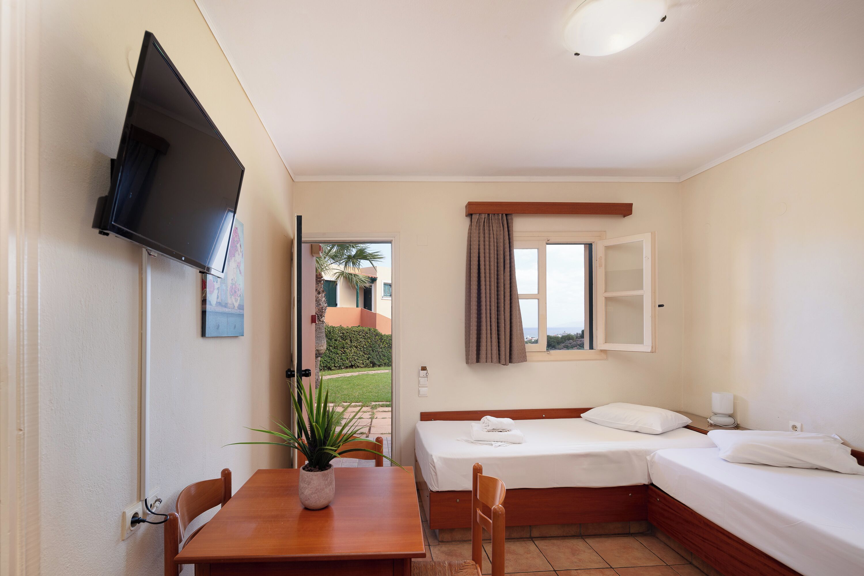 A small, clean room with a bed, a table, and a TV mounted on the wall.