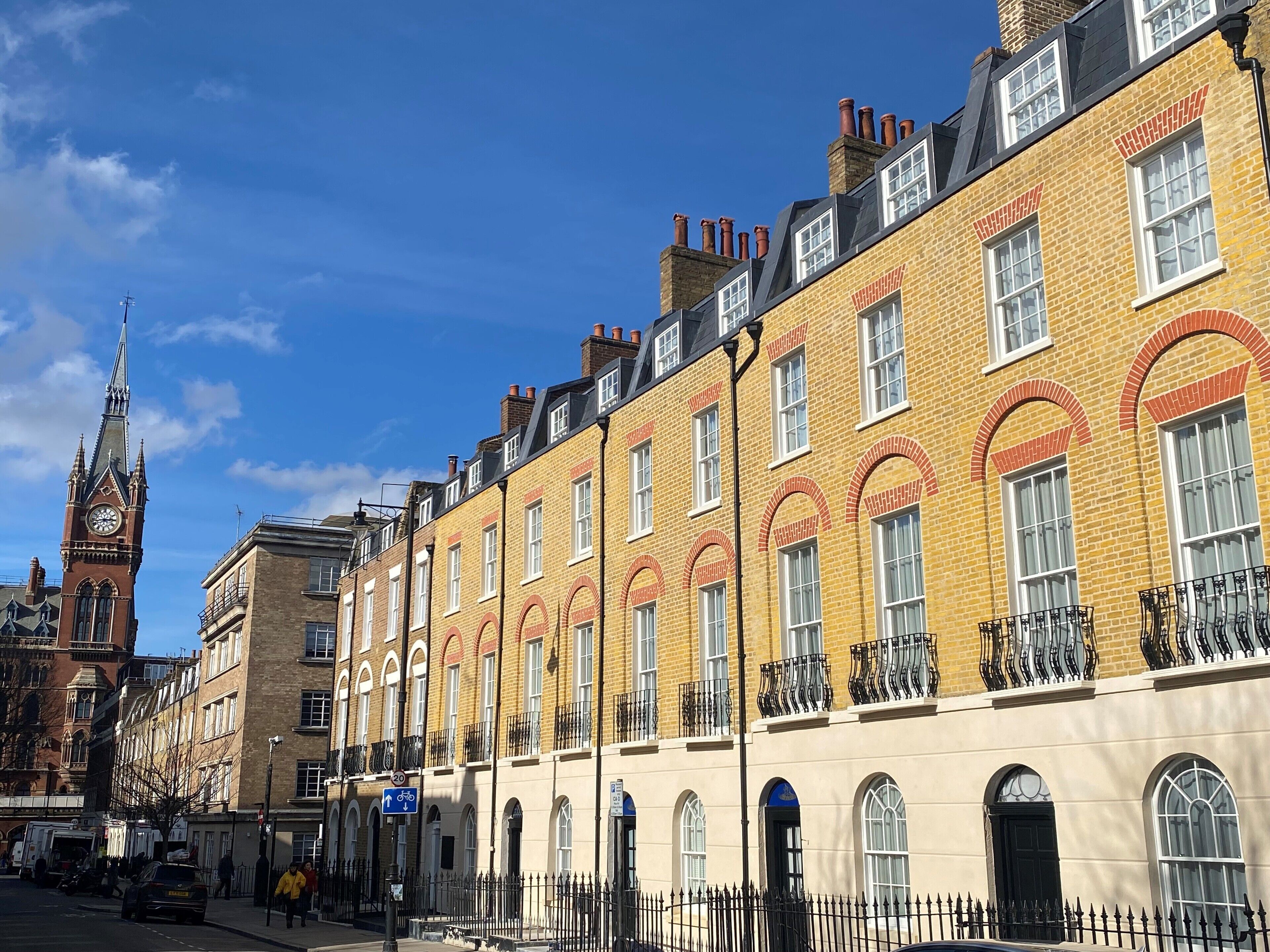 A row of yellow brick buildings with arched windows and a clock tower in the background.