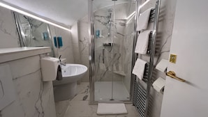 Un baño moderno con ducha de vidrio, un lavamanos blanco y piso de baldosas de mármol.