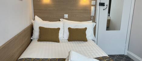 A hotel room with a wooden headboard, two white pillows, two brown pillows, a neatly made bed with a checkered bedspread, and a pair of folded towels on the floor.