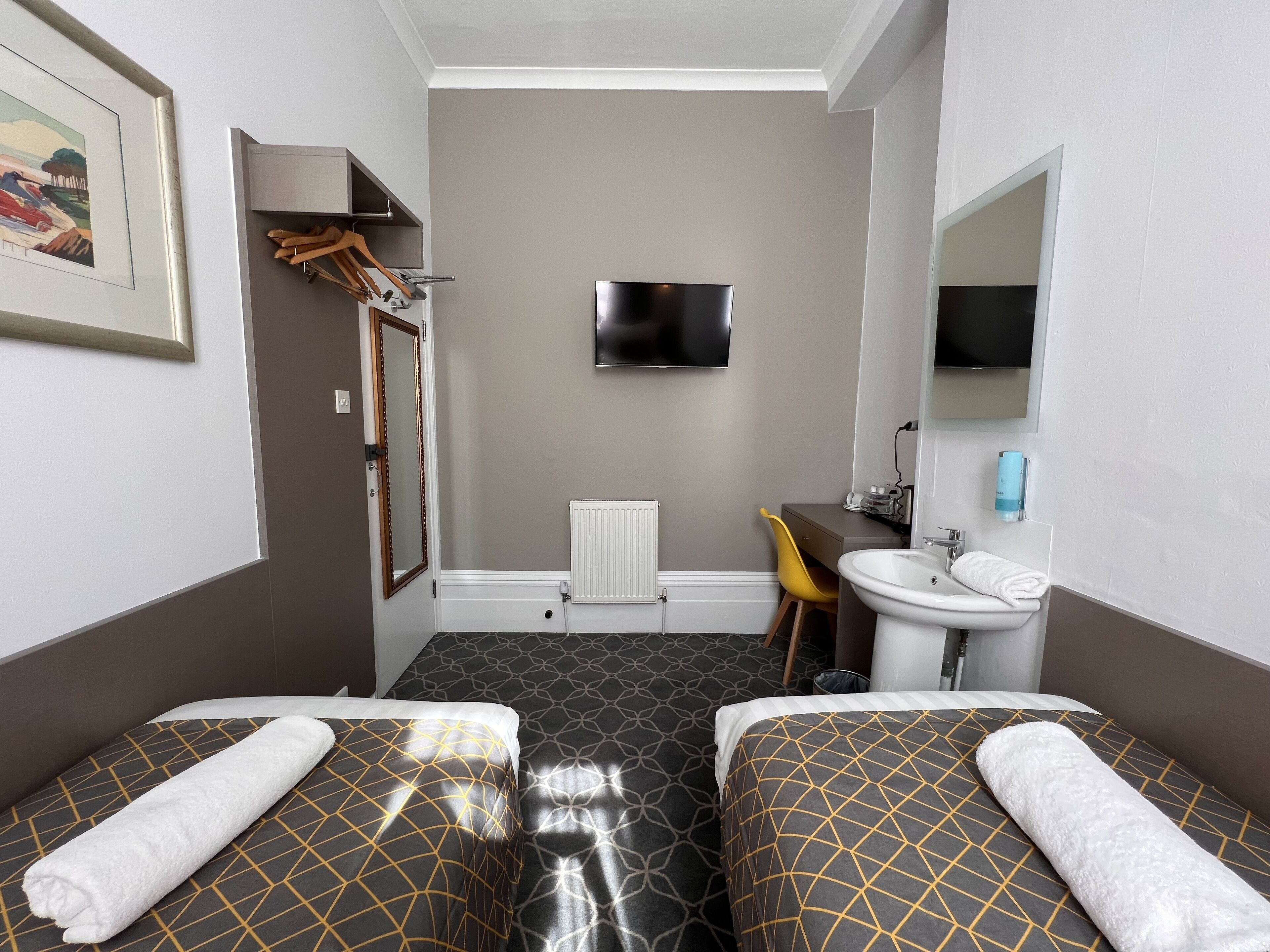 A hotel room with two beds, a TV, a sink, and a mirror.