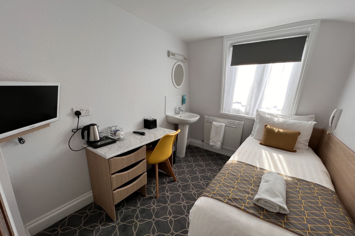 A hotel room with a bed, a desk with a chair, a sink, and a window with a view.