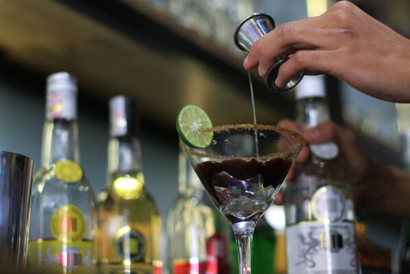 Un barman verse une boisson dans un verre à martini, qu’il garnit d’une tranche de citron vert.