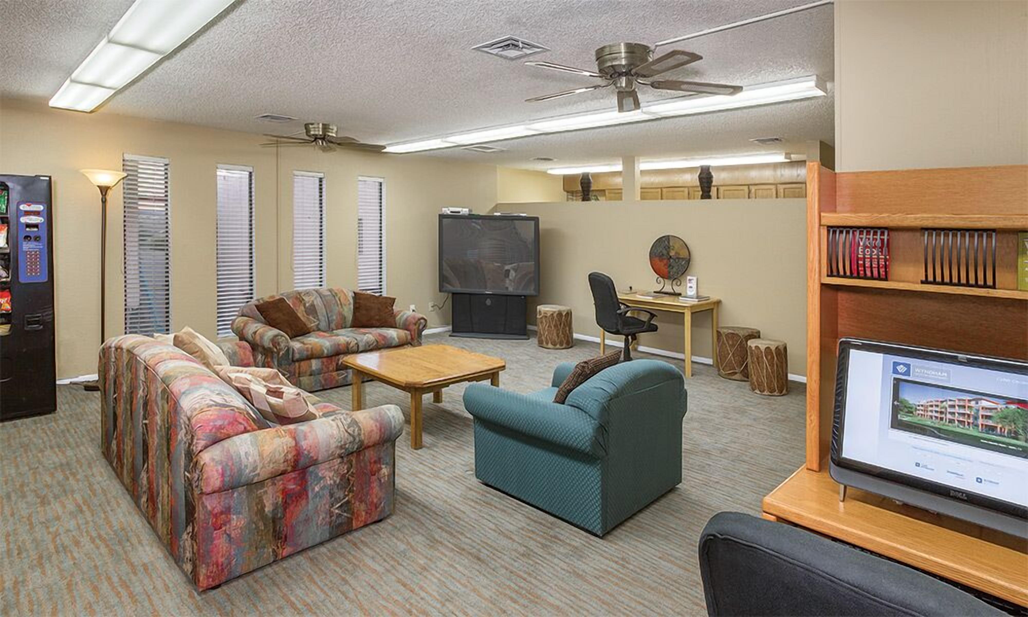 Una sala de estar con sofá, sillón, mesa de centro, televisión y monitor de computadora.