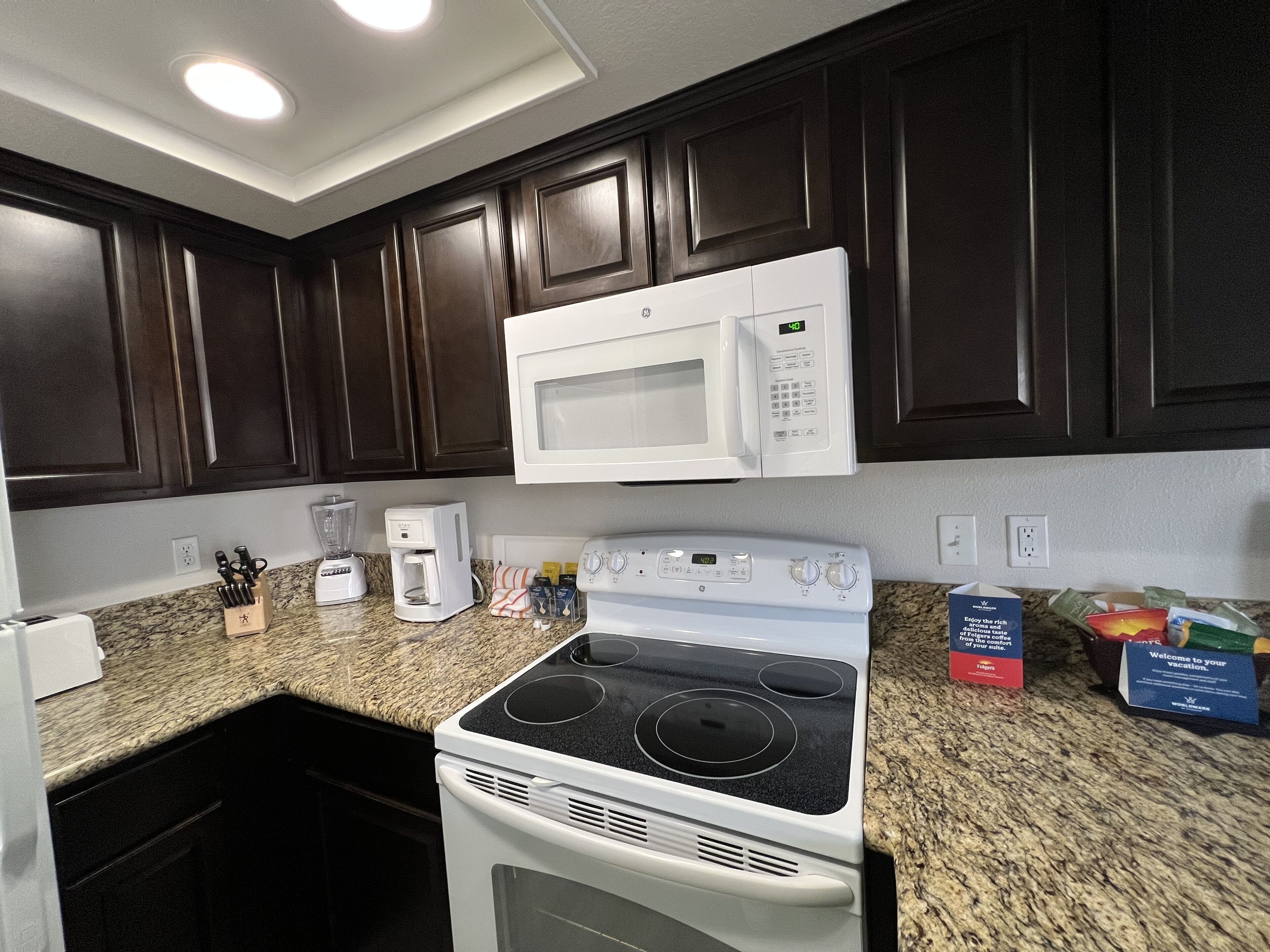 A kitchen with dark wooden cabinets, a white microwave, a stove, and a coffee maker.