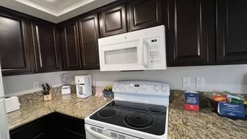 A kitchen with dark wooden cabinets, a white microwave, a stove, and a coffee maker.