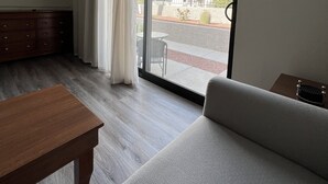 A modern hotel room with a large sliding glass door to the outside, a flat-screen TV mounted on the wall, a wooden dresser, and a grey sofa. - GetAways at Havasu Dunes Resort (Lake Havasu City)