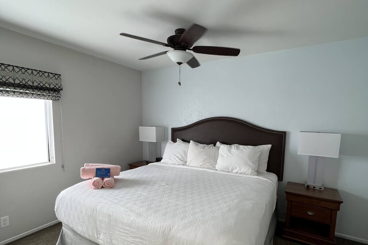 A neatly arranged hotel room with a large bed, two bedside tables with lamps, a ceiling fan, and a window with blinds.