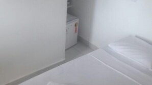 A hotel room with a neatly made bed, a small white cabinet, and a plain wall. - Recanto Tropical Hotel (Guarujá)