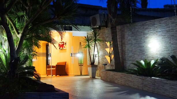 An outdoor area with a stone wall, palm trees, and a seating area with a bench and a table. - Recanto Tropical Hotel (Guarujá)