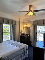 Habitación de hotel con cama, tocador con espejo, ventilador de techo y vistas al exterior.