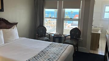 Una habitación de hotel con cama, escritorio, silla, ventana con vista al océano y ventilador de techo.