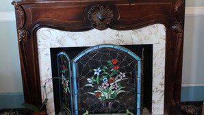 A fireplace with a stained glass door, a framed painting of a ship, and two potted plants. - Studio 9 Hotel Catalina (Avalon)