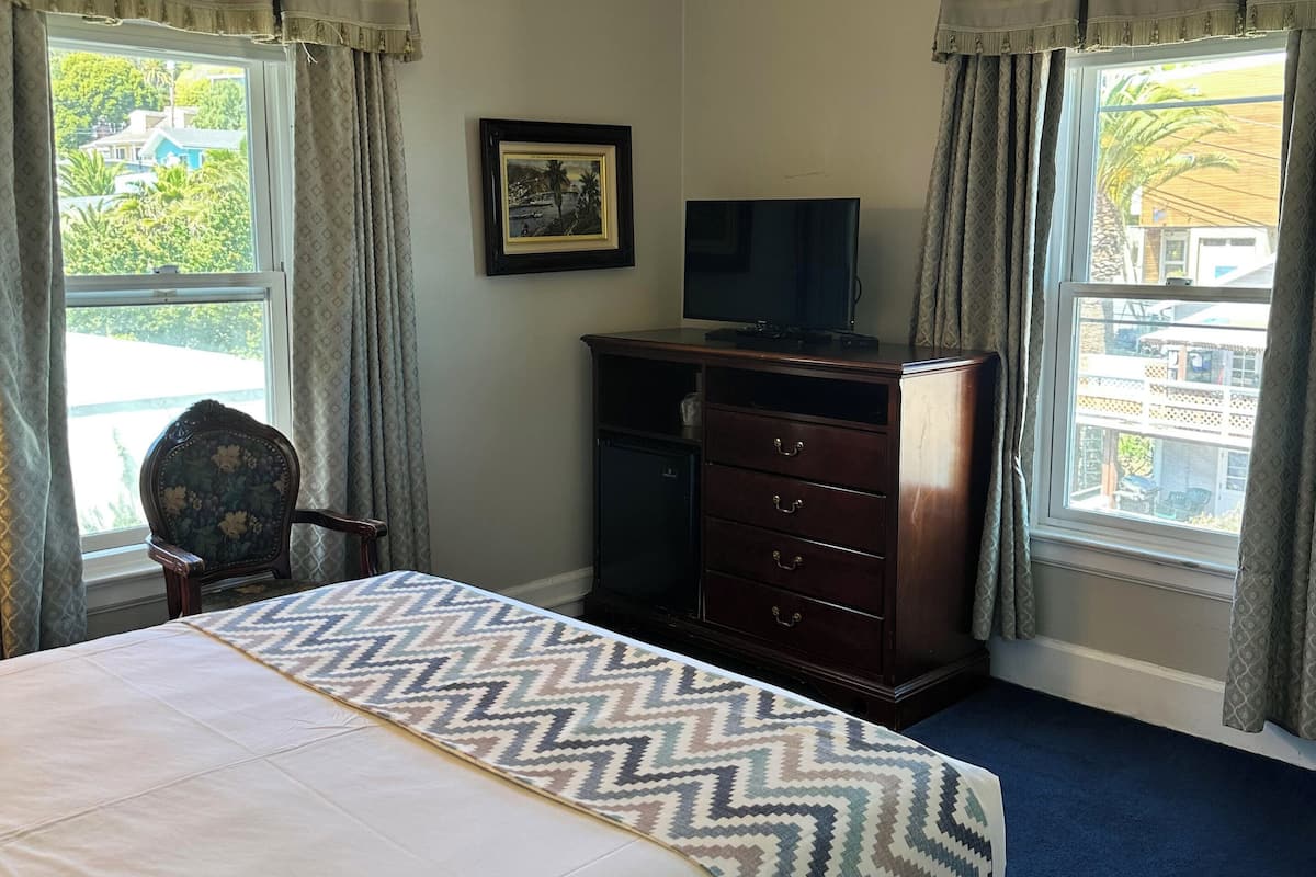 A bedroom with a bed, a dresser, a chair, a ceiling fan, and a TV.