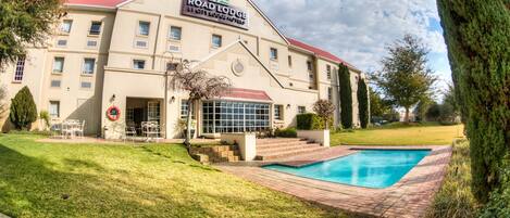 A hotel with a swimming pool, a red roof, and a sign that reads "Road Lodge by City Lodge Hotels".