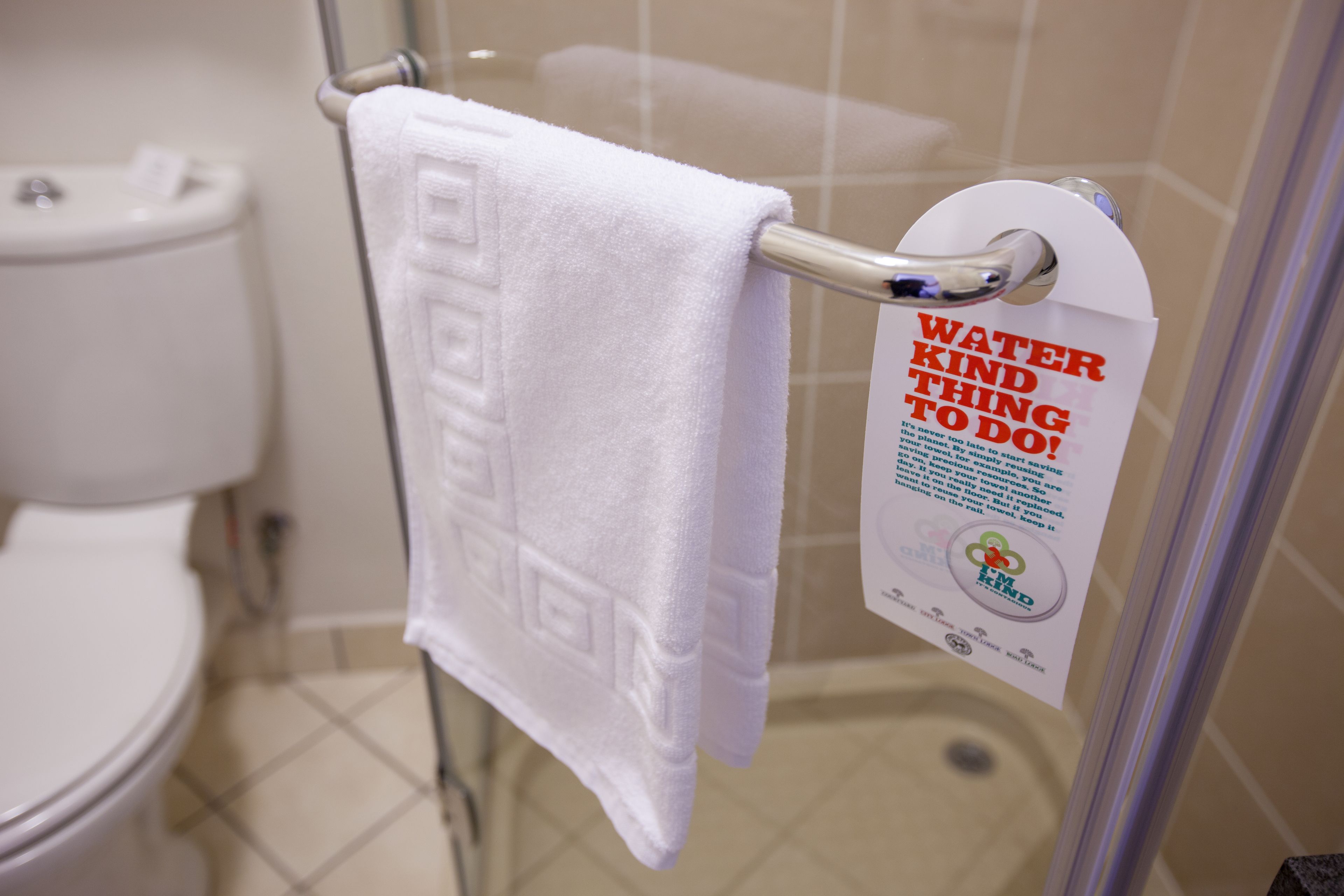 A bathroom with a white towel hanging on a metal rack, a white toilet, and a sign promoting water conservation.