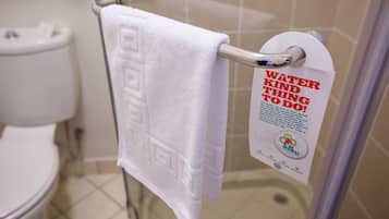 A bathroom with a white towel hanging on a metal rack, a white toilet, and a sign promoting water conservation.