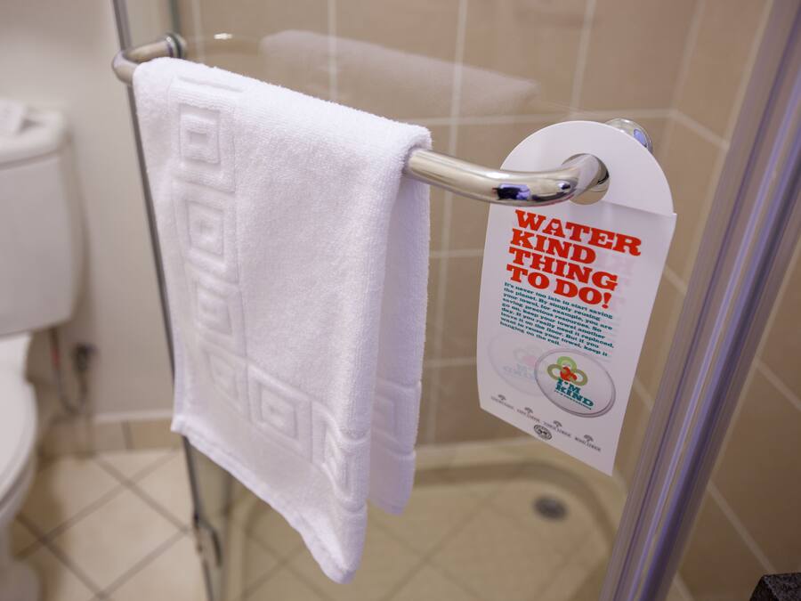 A bathroom with a white towel hanging on a metal rack, a white toilet, and a sign promoting water conservation.