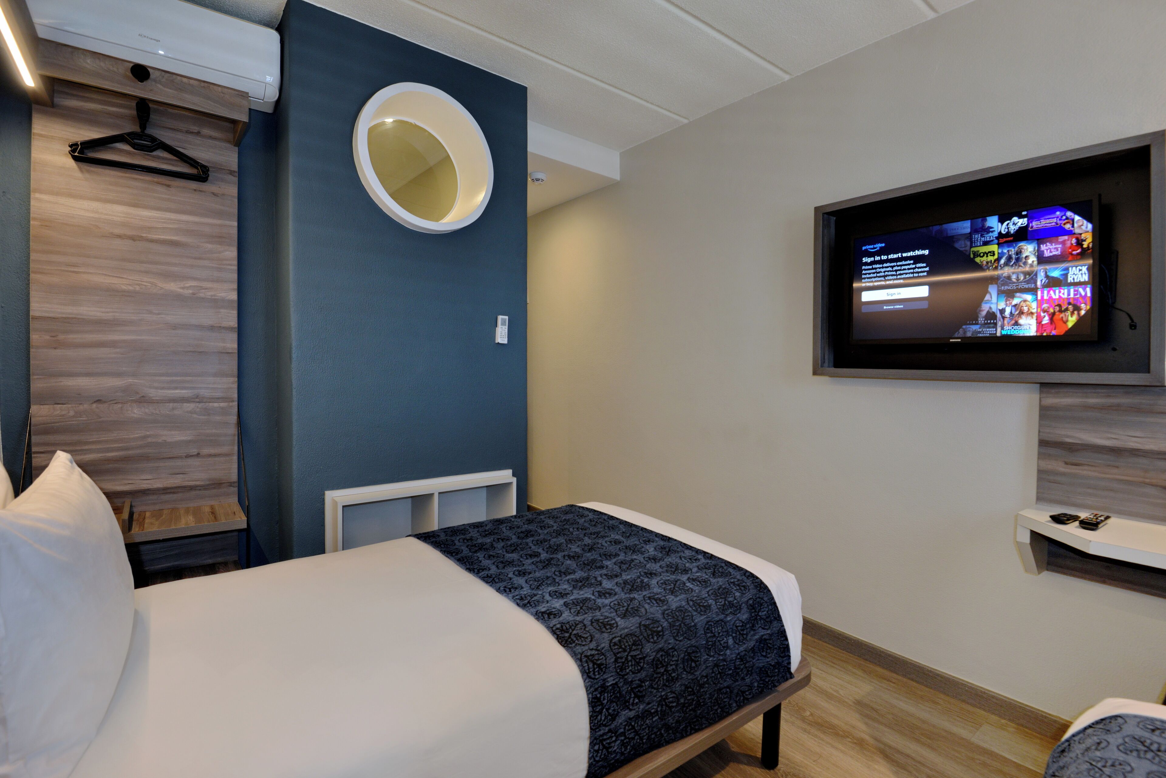Una habitación de hotel moderna con una cama, un televisor montado en la pared, un espejo circular y un cabecero de madera.