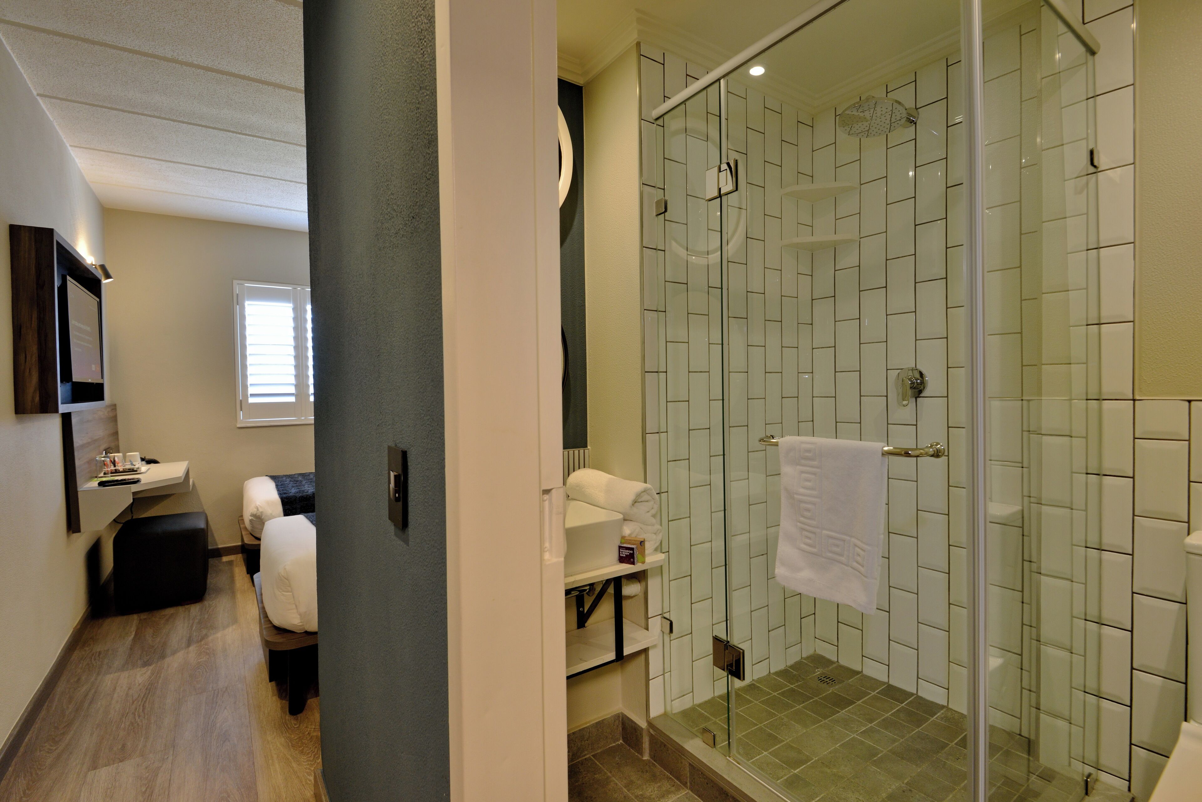 Een moderne badkamer met een douchecabine van glas, een wastafel met spiegel en een klein zitgedeelte met een bankje.