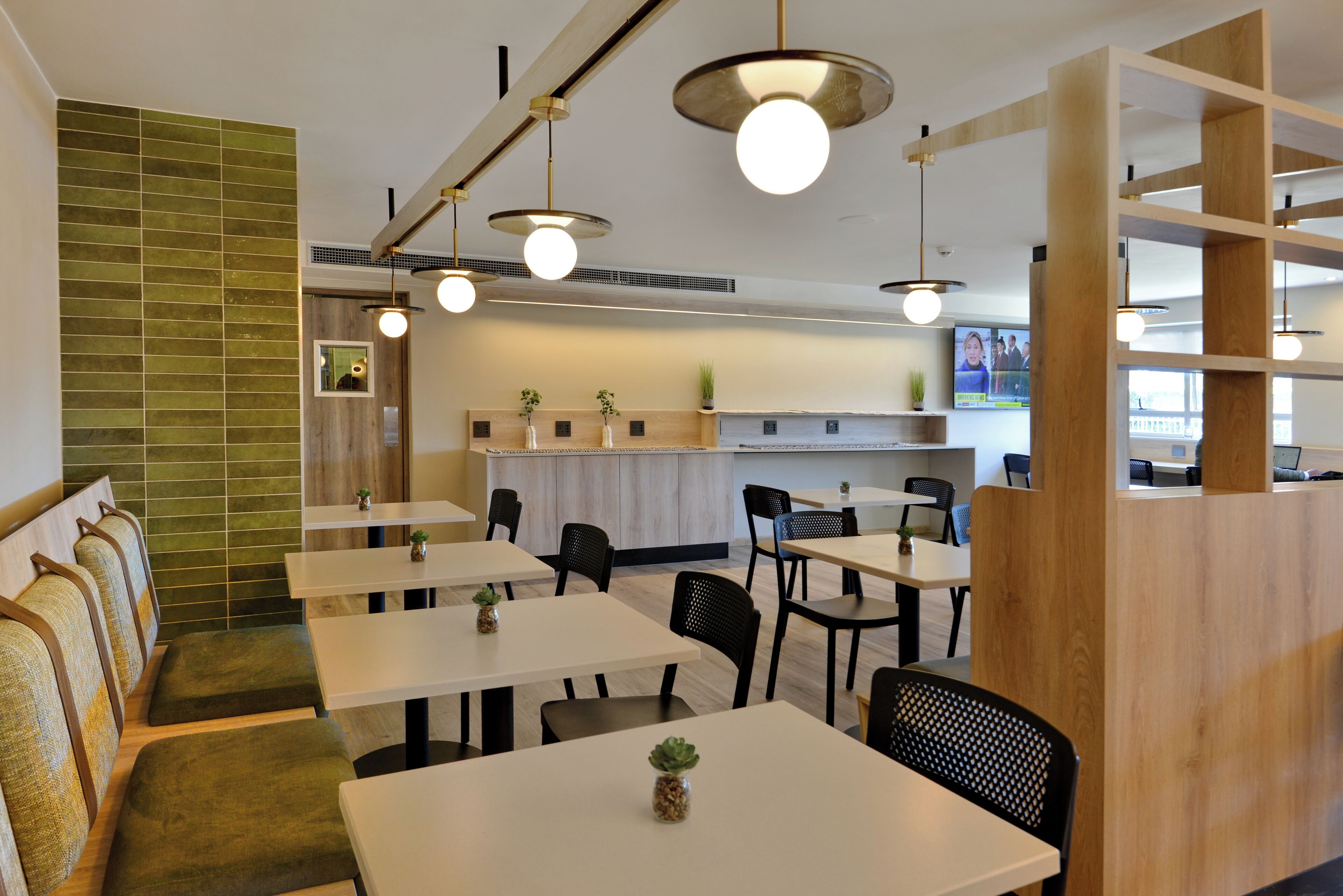 Un restaurante moderno con mesas blancas y sillas negras, asientos acolchados verdes y detalles de madera.