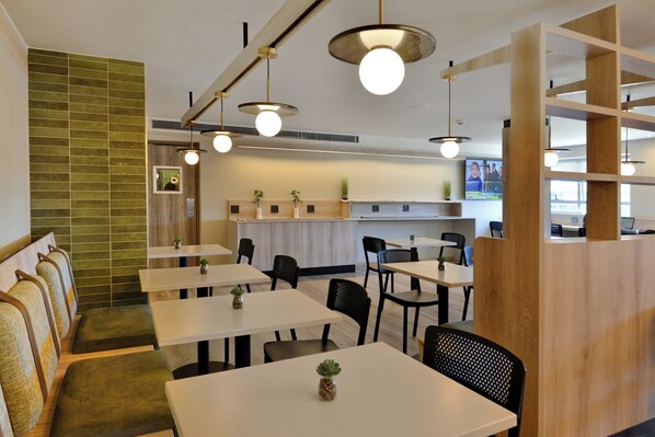 Un restaurante moderno con mesas blancas y sillas negras, asientos acolchados verdes y detalles de madera.