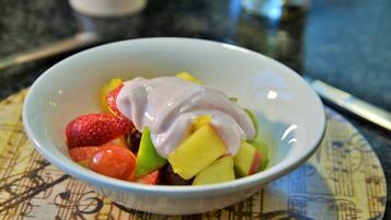 Un saladier rempli de salade de fruits, avec des fraises, de la mangue et une cuillère de yaourt, posé sur une nappe à motifs.