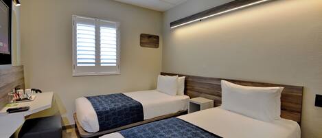A hotel room with two beds, a desk, and a window.