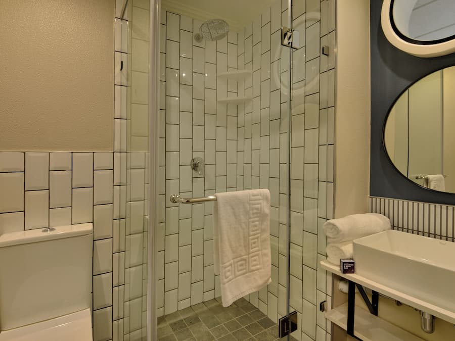 A bathroom with a glass-enclosed shower, white tiles, a white sink, and a round mirror.