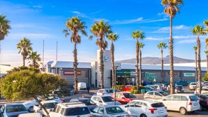 A parking lot with multiple cars, palm trees, and a building with signage for 'Checker' and 'House & Home'. - Road Lodge N1 City (Cape Town)
