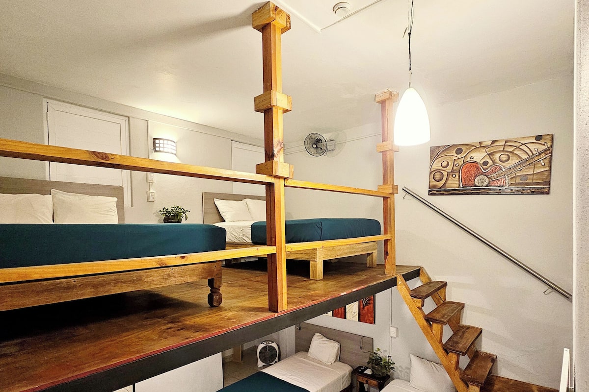 Habitación tipo dormitorio con literas, una escalera y una pequeña zona de estar.