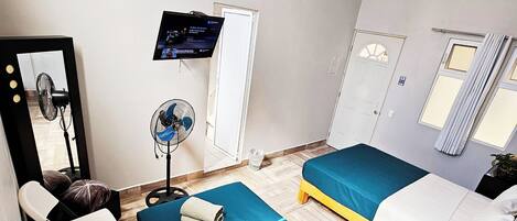 Habitación de hotel con dos camas, un escritorio, una silla, un televisor y un ventilador.